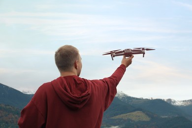 Young man with modern drone in mountains, back view