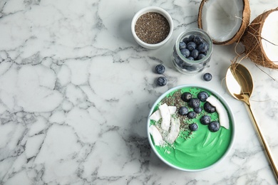 Flat lay composition with bowl of spirulina smoothie and space for text on marble background