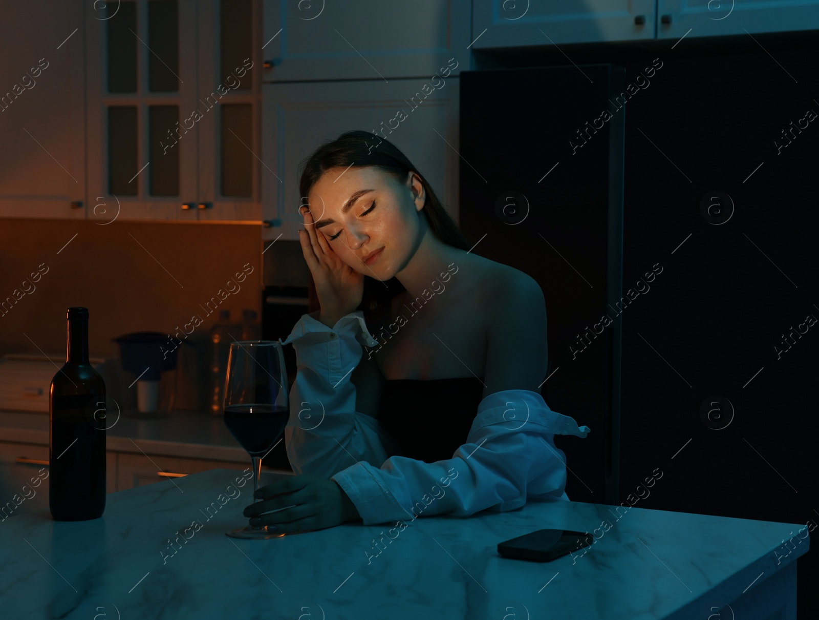 Photo of Beautiful woman chilling with glass of wine in kitchen at night