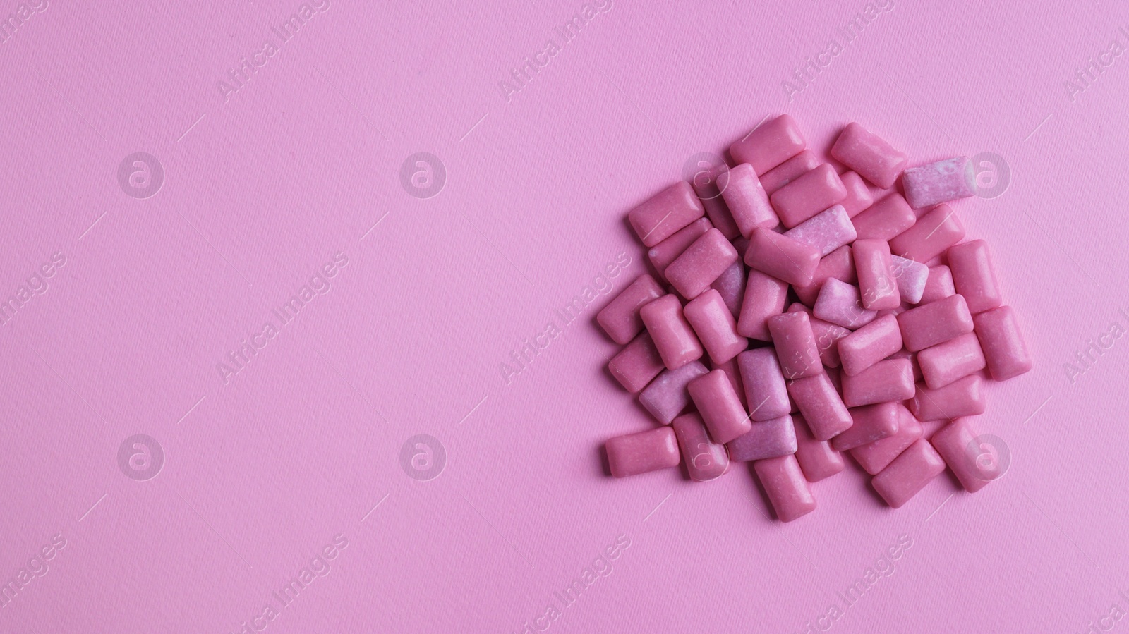 Photo of Heap of tasty sweet chewing gums on pink background, flat lay. Space for text