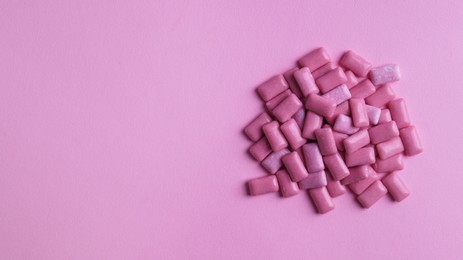 Photo of Heap of tasty sweet chewing gums on pink background, flat lay. Space for text