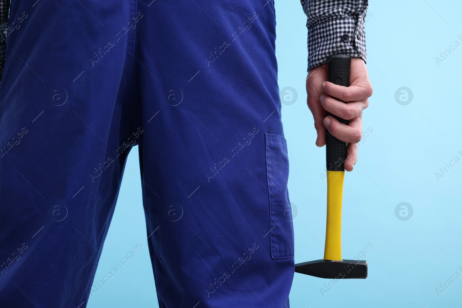 Photo of Professional repairman holding hammer on light blue background, closeup