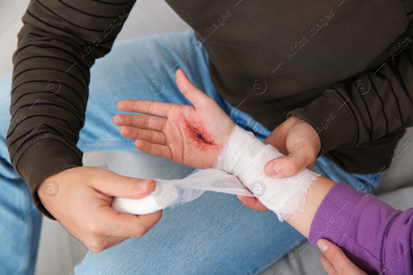 Photo of Young man applying bandage on woman's injured hand at home, closeup. First aid