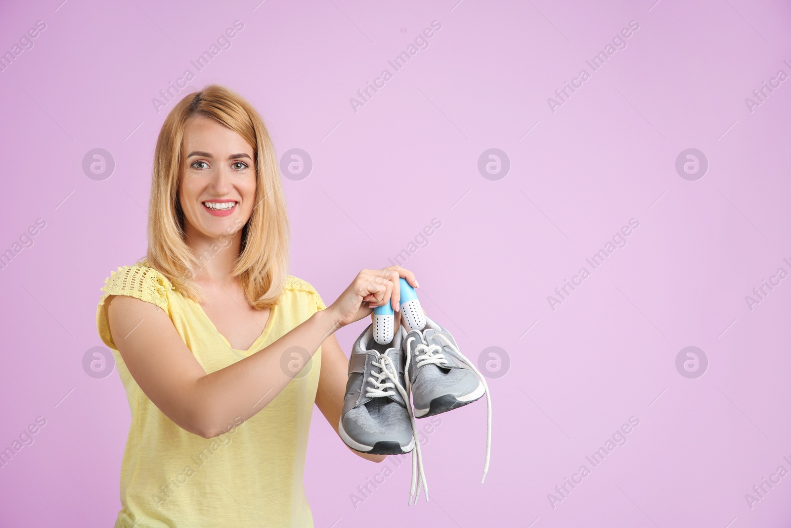 Photo of Young woman putting capsule air fresheners in shoes on color background