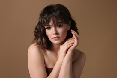 Portrait of beautiful young woman with wavy hairstyle on brown background