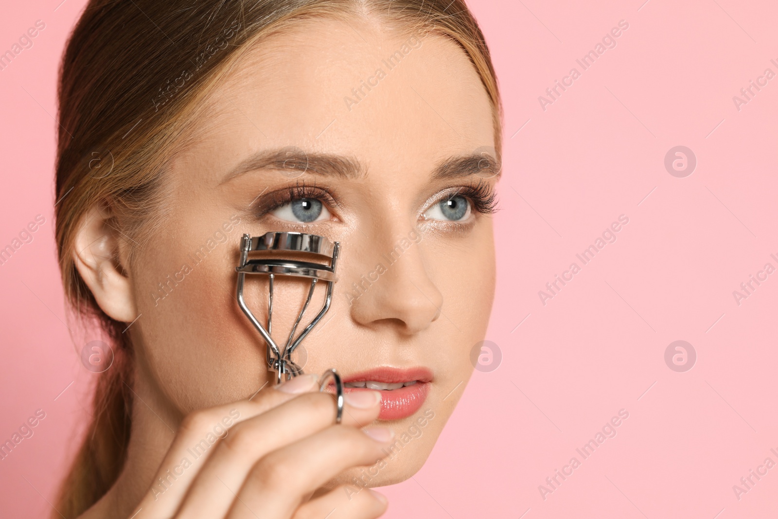 Photo of Young woman with eyelash curler on pink background, space for text