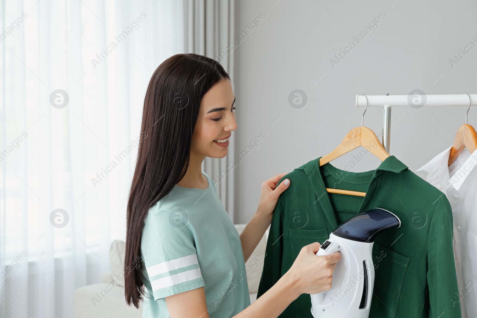 Photo of Woman steaming shirt on hanger at home