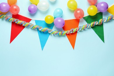 Bunting with colorful triangular flags and other festive decor on light blue background, flat lay. Space for text