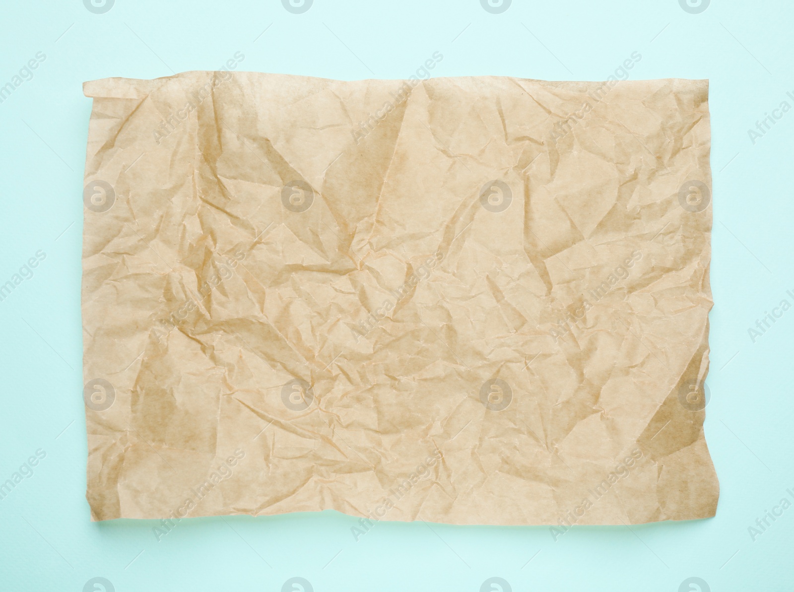 Photo of Sheet of crumpled brown baking paper on light blue background, top view