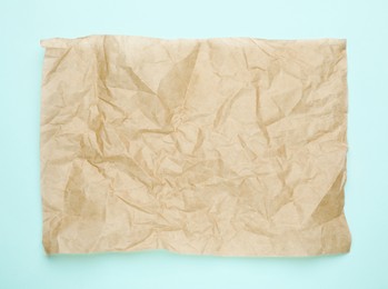 Photo of Sheet of crumpled brown baking paper on light blue background, top view