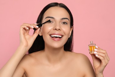 Photo of Young woman applying oil onto eyelashes on pink background