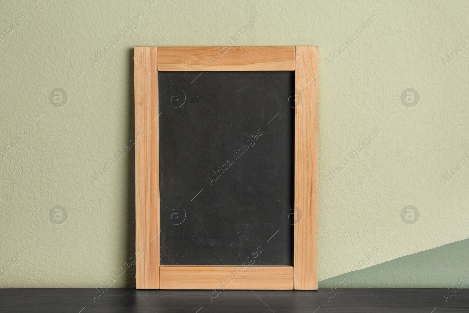 Photo of Small clean chalkboard on table near color wall
