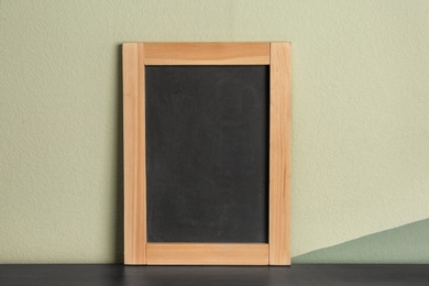 Small clean chalkboard on table near color wall