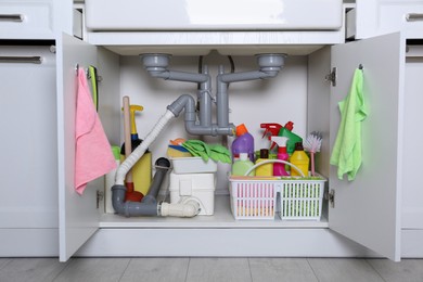 Photo of Open under sink cabinet with different cleaning supplies in kitchen