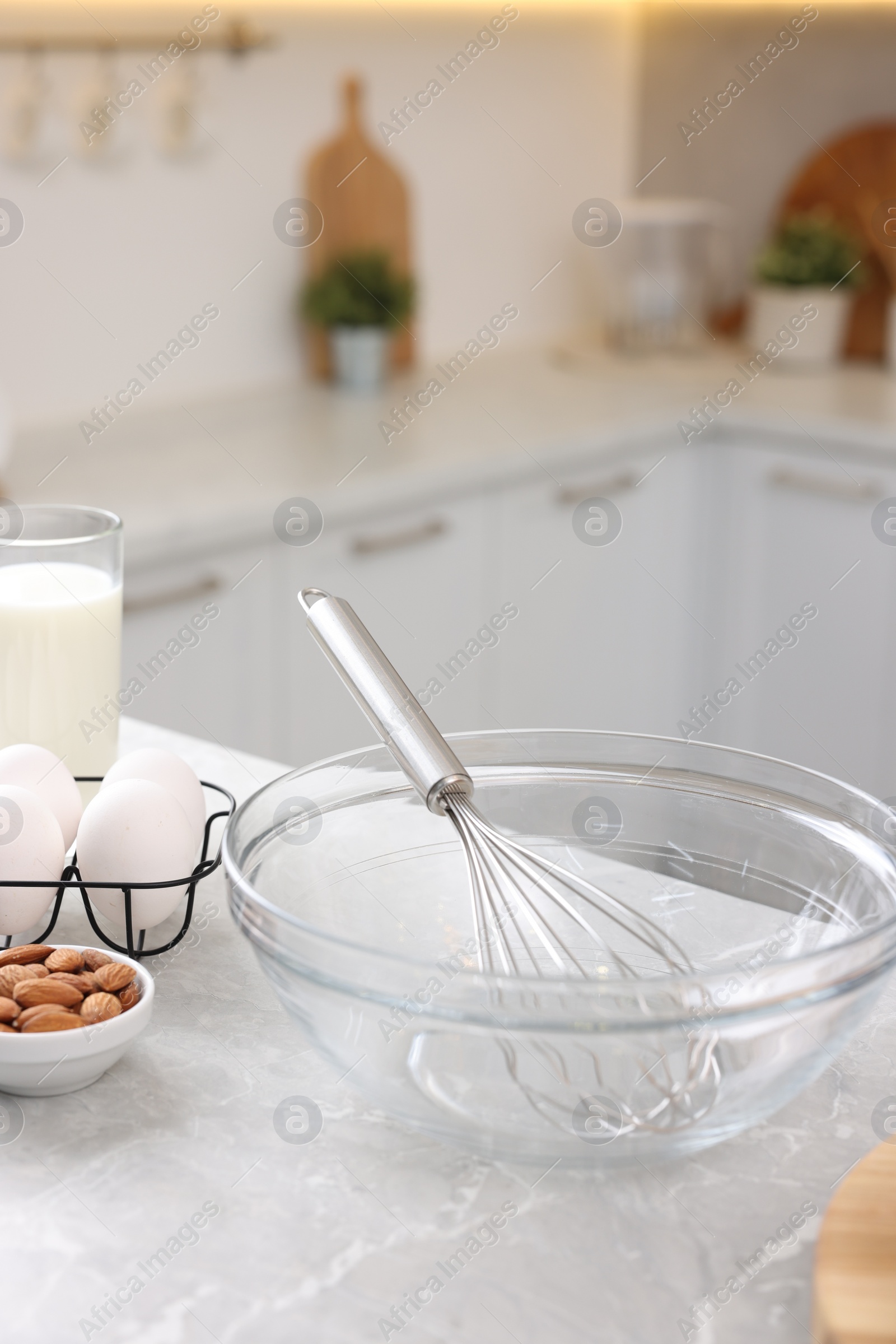 Photo of Metal whisk, bowl and different products on gray marble table in kitchen