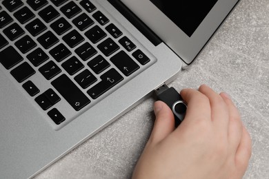 Photo of Woman attaching usb flash drive into laptop at grey table, closeup
