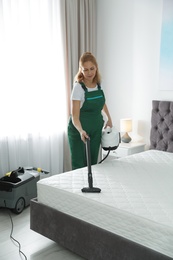 Janitor cleaning mattress with professional equipment in bedroom