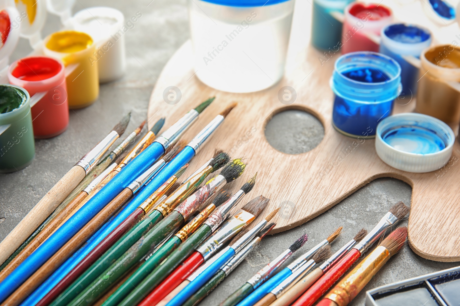 Photo of Different paints, brushes and palette on grey  table, closeup