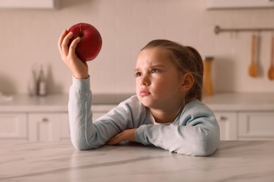 Photo of Cute little girl refusing to eat apple in kitchen