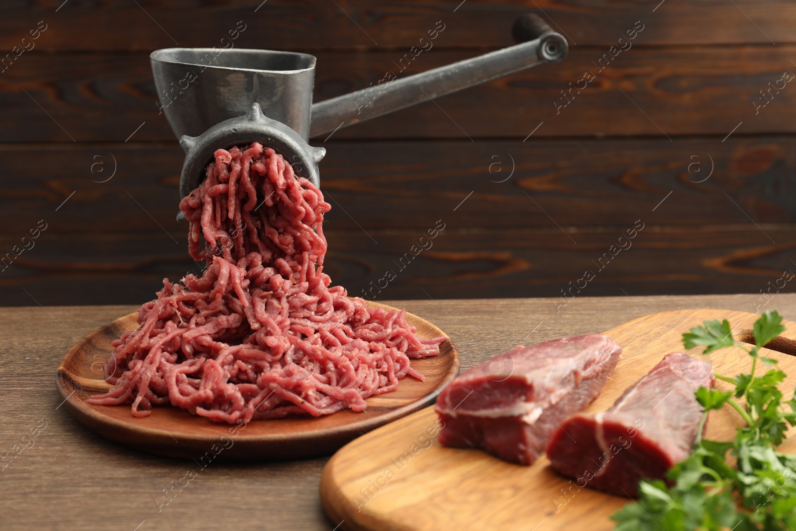 Photo of Manual meat grinder with beef and parsley on wooden table