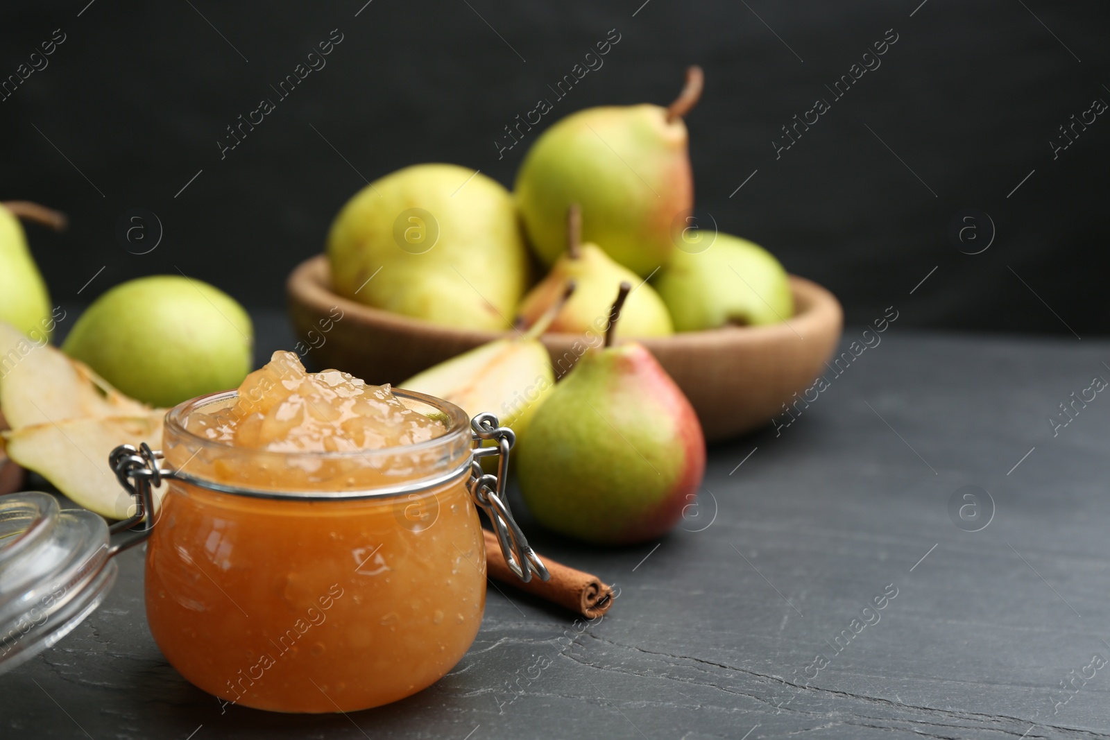 Photo of Tasty homemade pear jam and fresh fruits on black table. Space for text