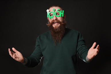 Photo of Bearded man in party glasses on black background. St. Patrick's Day celebration