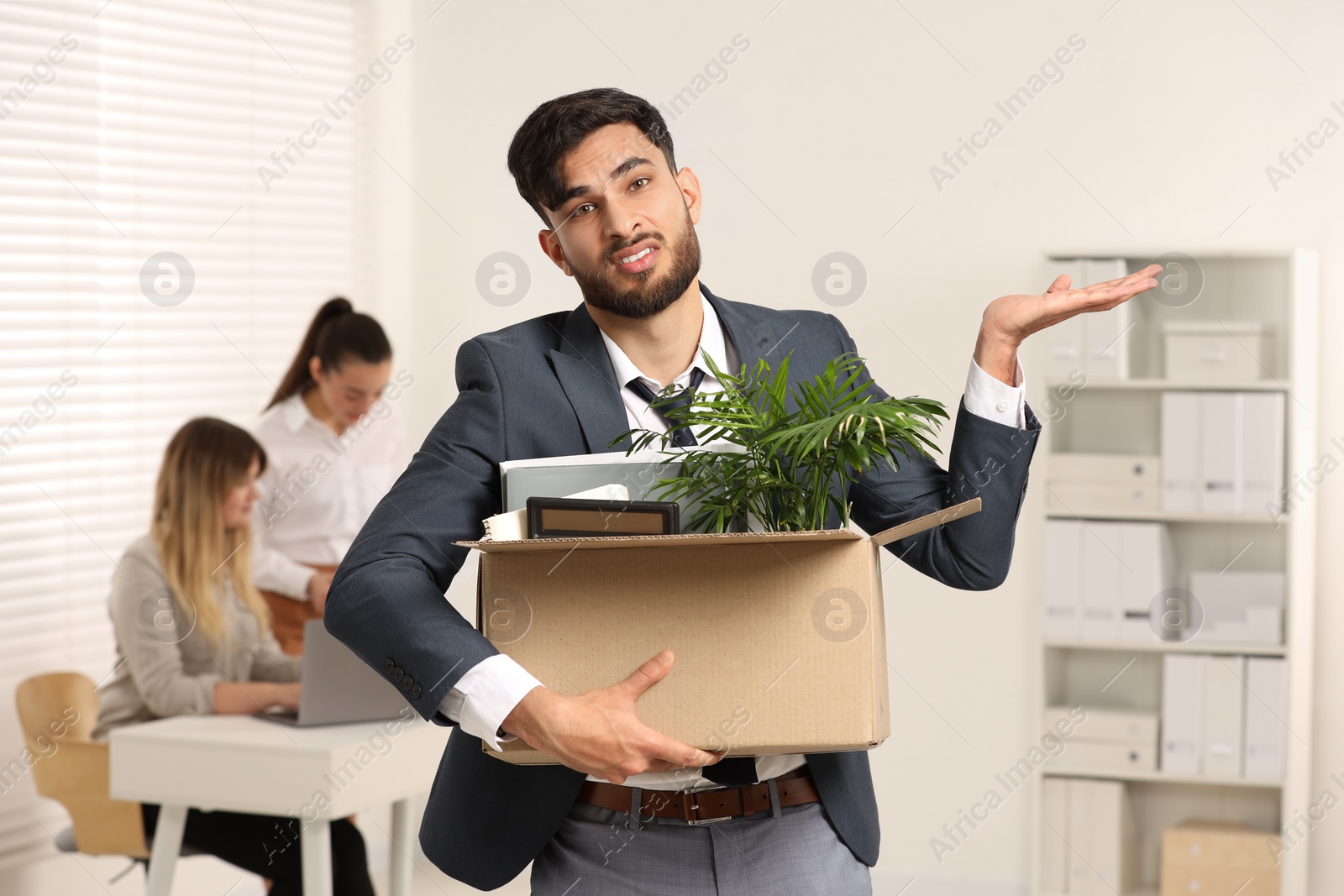 Photo of Unemployment problem. Frustrated man with box of personal belongings in office