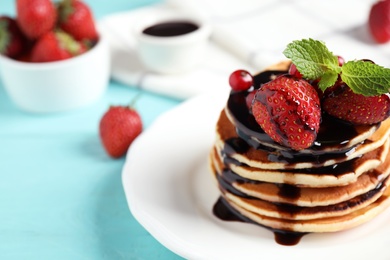 Photo of Delicious pancakes with fresh strawberries and chocolate on light blue wooden table