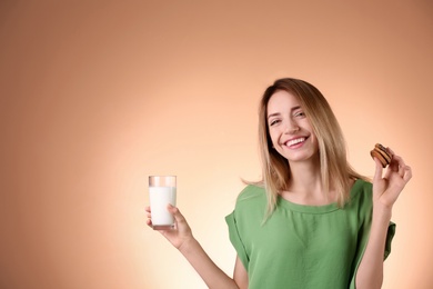 Photo of Beautiful young woman drinking milk with cookies on color background