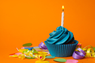 Delicious birthday cupcake with blue cream and burning candle on orange background