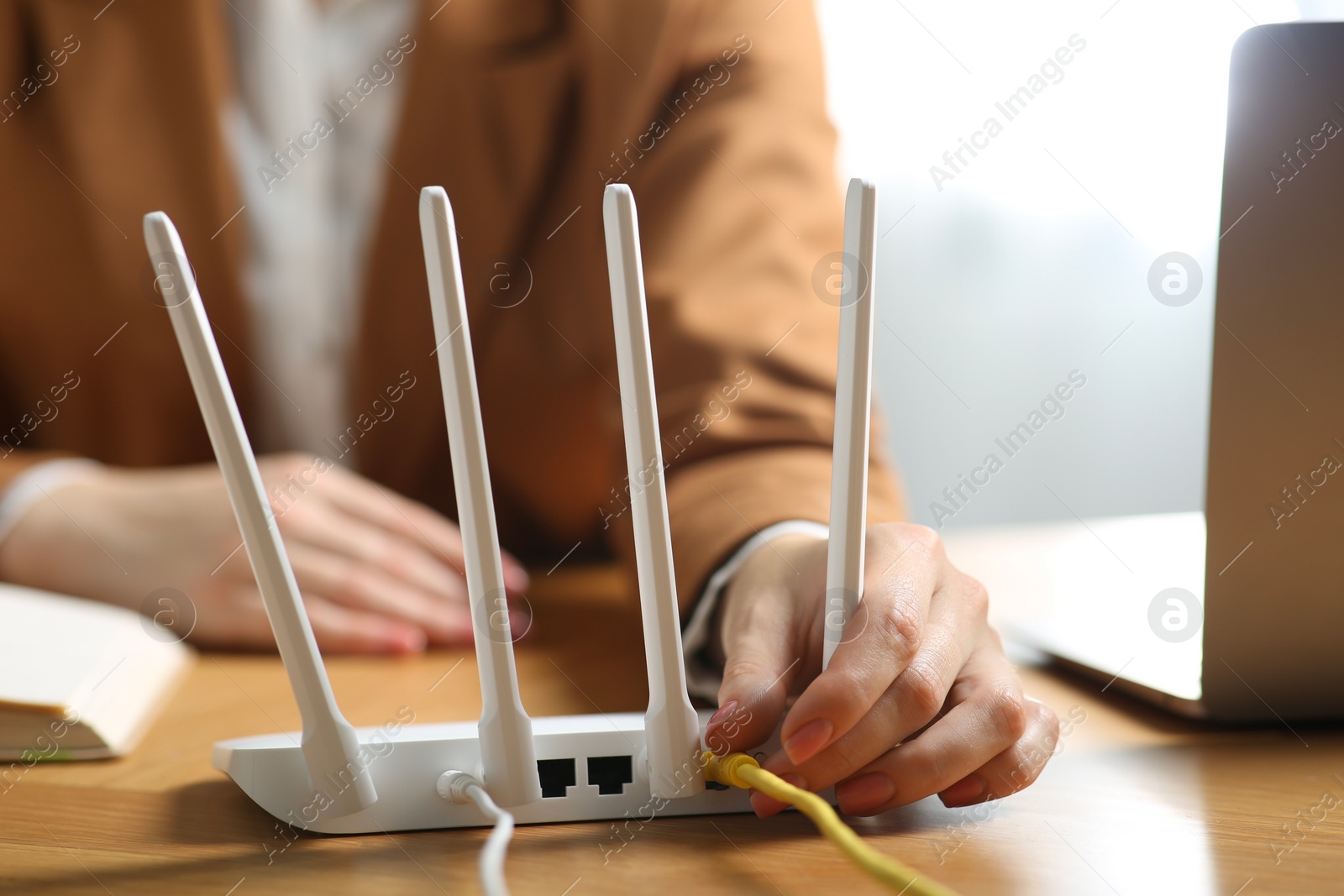 Photo of Woman connecting cable to Wi-Fi router at table indoors, closeup