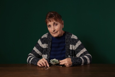 Poor senior woman with money at table against color background