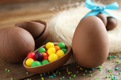 Photo of Tasty chocolate eggs with colorful candies on wooden table, closeup