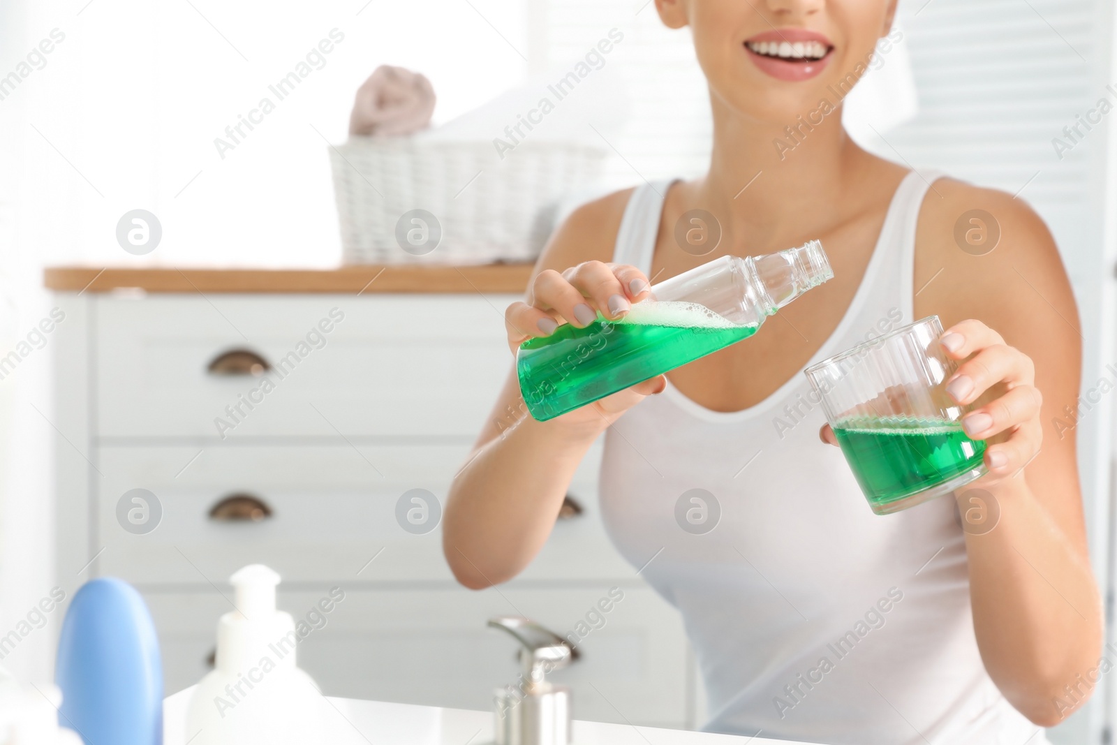 Photo of Woman pouring mouthwash from bottle into glass, closeup. Teeth care