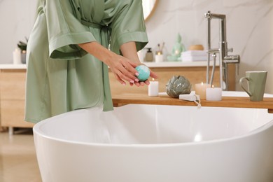 Photo of Young woman holding bath bomb over tub in bathroom, closeup