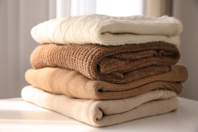 Stack of folded warm sweaters on white table indoors, closeup