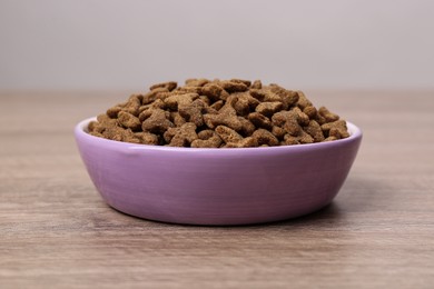 Dry food in violet pet bowl on wooden surface