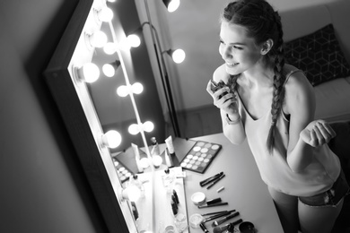 Photo of Portrait of beautiful woman with natural makeup applying perfume near mirror indoors, black and white effect