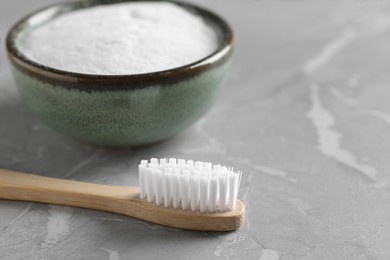 Photo of Bamboo toothbrush and bowl of baking soda on light gray marble table, closeup
