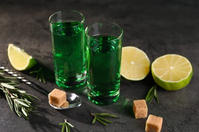 Absinthe in shot glasses, spoon, brown sugar, lime and rosemary on gray textured table, closeup. Alcoholic drink