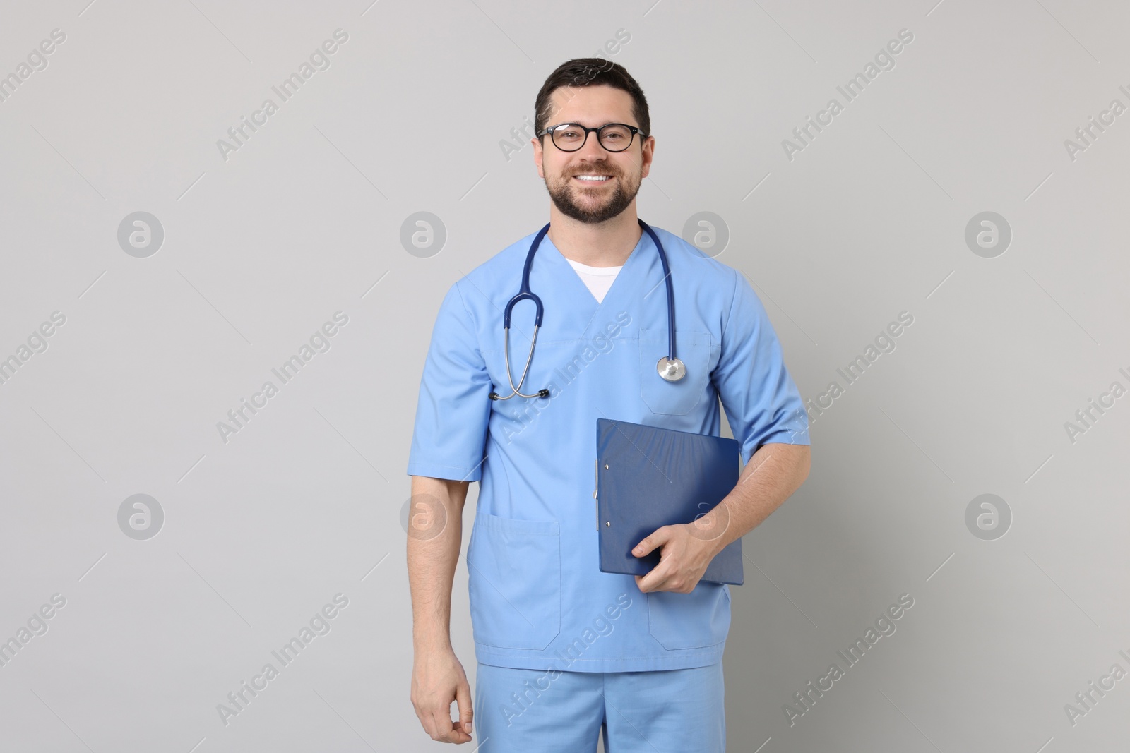 Photo of Smiling doctor with clipboard on light grey background