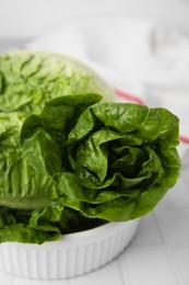 Photo of Bowl with fresh green romaine lettuces on white tiled table, closeup