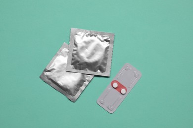 Contraception choice. Pills and condoms on turquoise background, flat lay