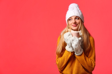 Portrait of emotional young woman in stylish clothes with cup on color background, space for text. Winter atmosphere