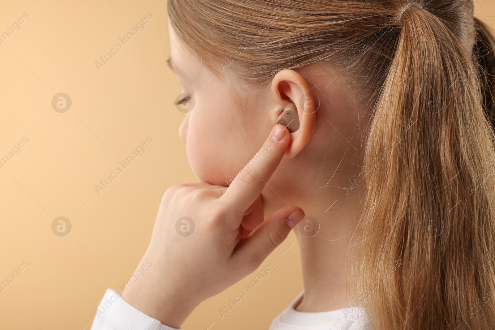 Photo of Little girl with hearing aid on pale brown background, closeup