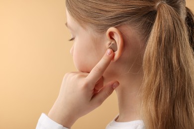 Photo of Little girl with hearing aid on pale brown background, closeup