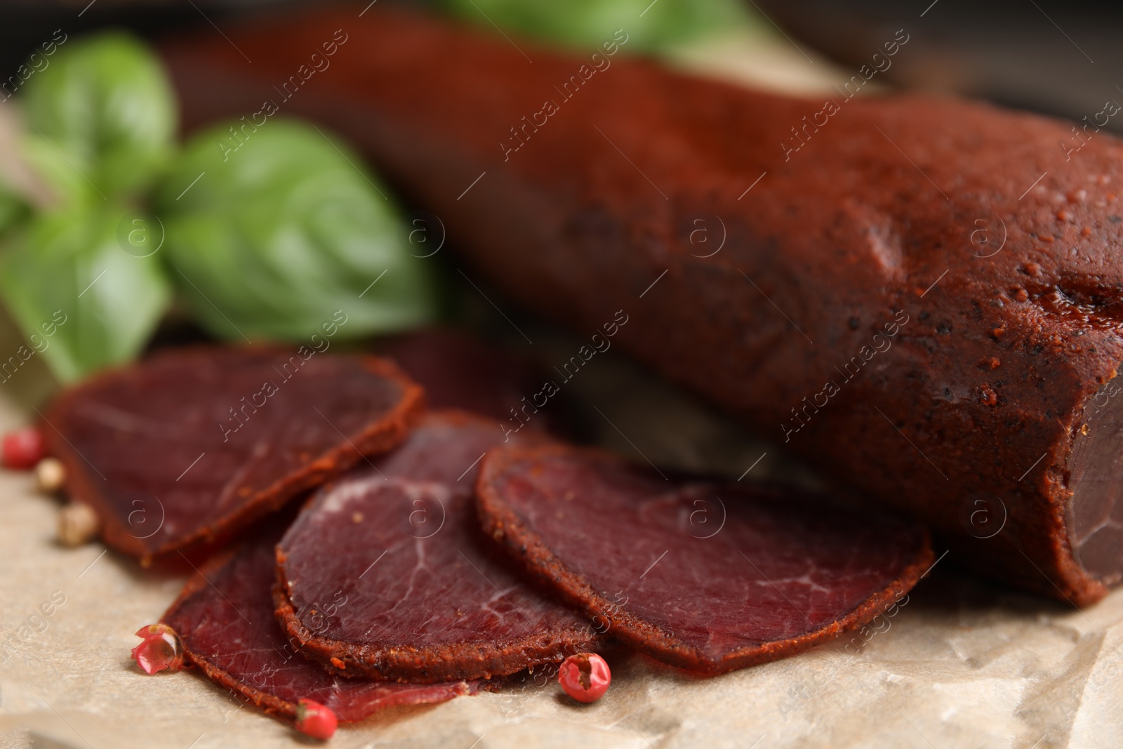 Photo of Delicious dry-cured beef basturma with basil and peppercorns on table, closeup