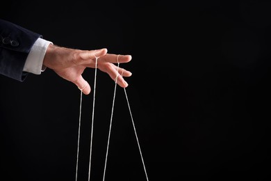 Photo of Man pulling strings of puppet on black background, closeup. Space for text
