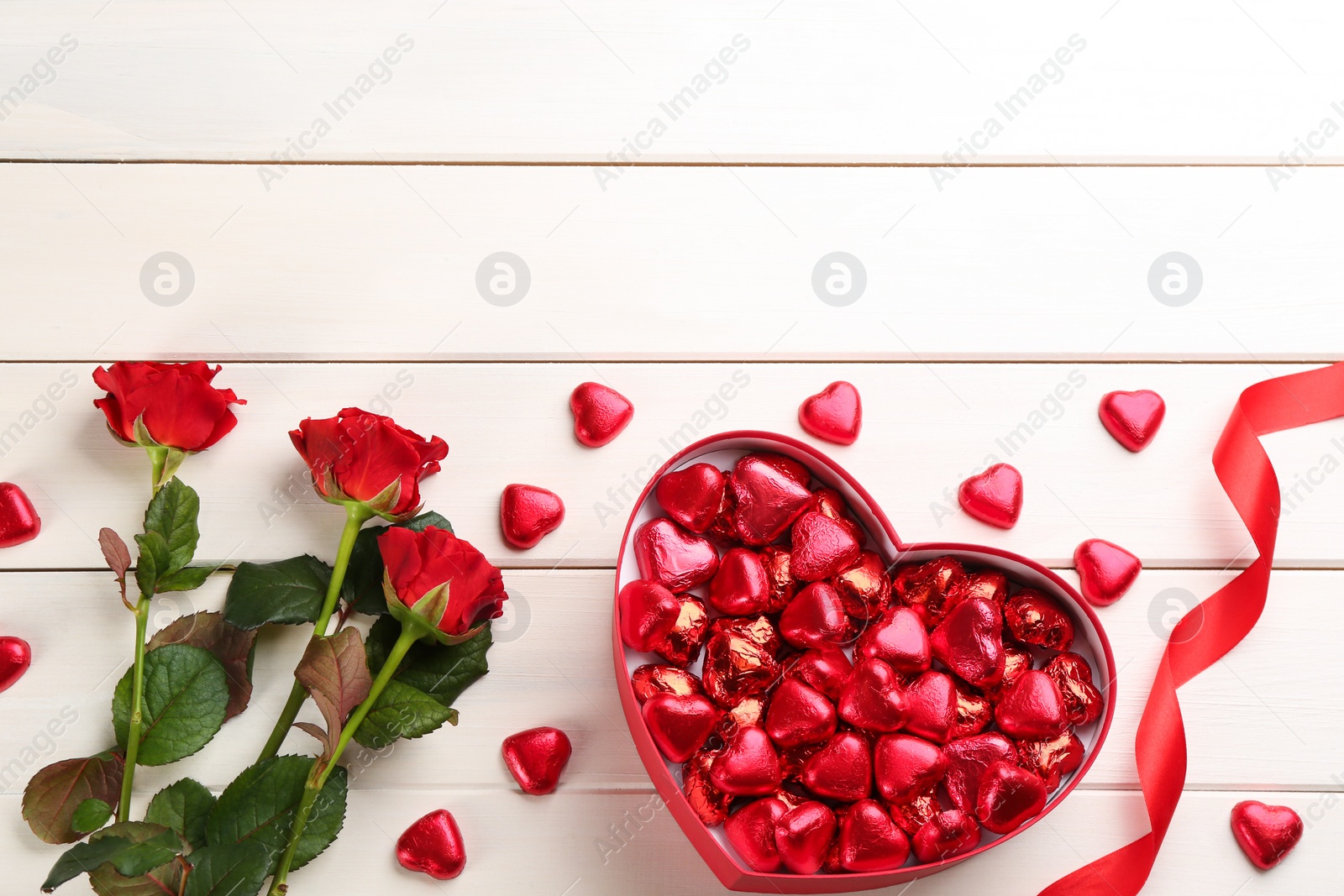 Photo of Heart shaped chocolate candies and bouquet on white wooden table, flat lay. Space for text