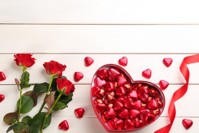 Heart shaped chocolate candies and bouquet on white wooden table, flat lay. Space for text